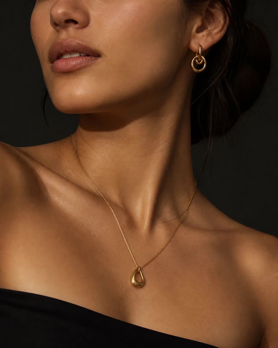Close-up of a woman wearing a delicate gold necklace and sculptural earrings